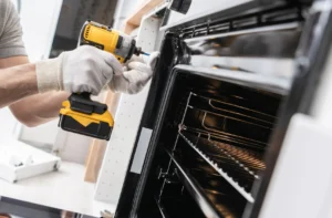 a person is using a cordless drill to repair an oven.