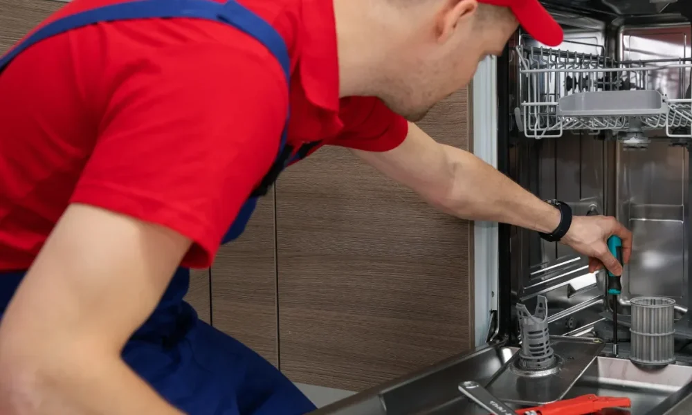 a person is fixing a dishwasher in the kitchen.
