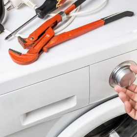 a person is holding a pair of pliers next to a washing machine.