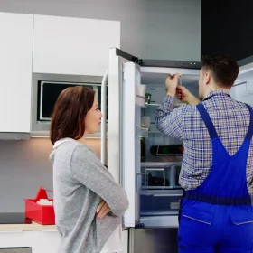 Two people standing in front of a refrigerator.